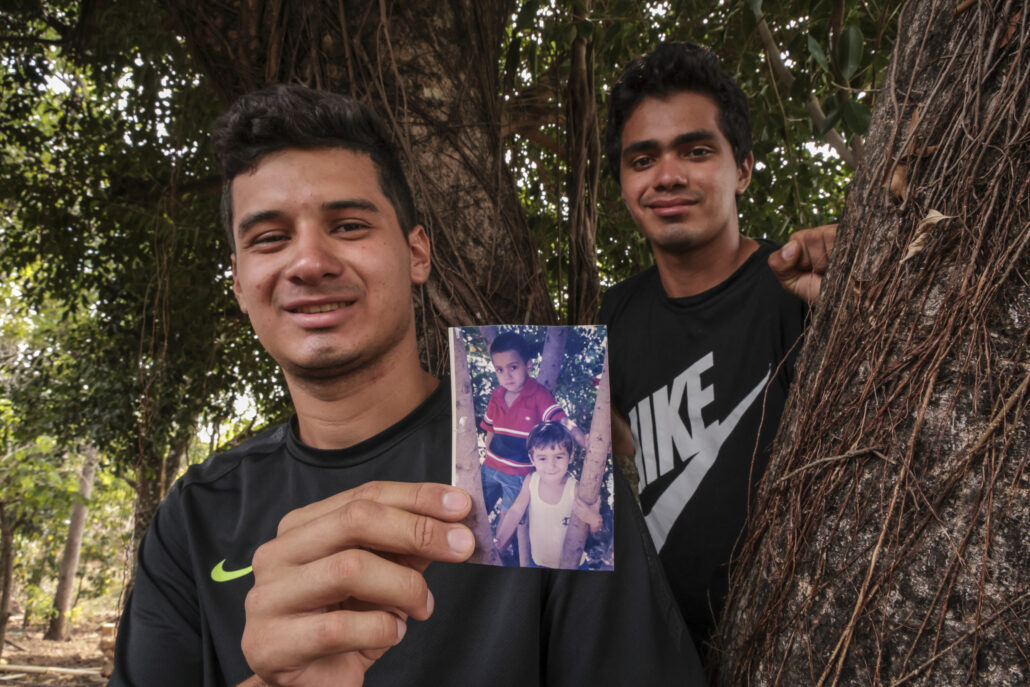 Dos jóvenes sonrientes sostienen una fotografía de cuando eran niños.