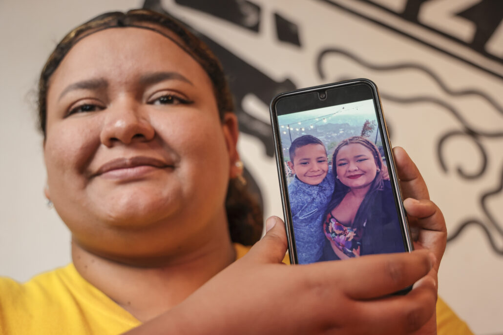 Maydeline sostiene un teléfono móvil con una fotografía de ella y su hijo Mauricio, mostrando con orgullo la imagen en la pantalla.